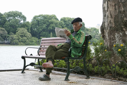 Một cụ gia đọc báo ngồi hưởng thụ cái lạnh ngay cạnh bờ hồ